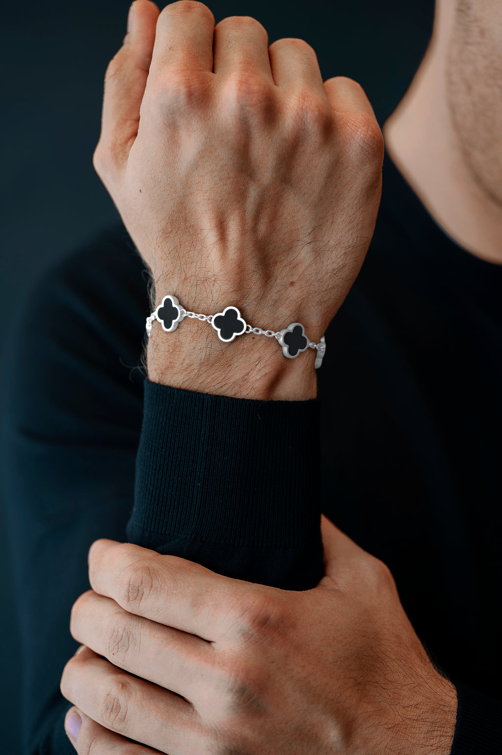 Person wearing a bracelet with clover-shaped charms on a dark background