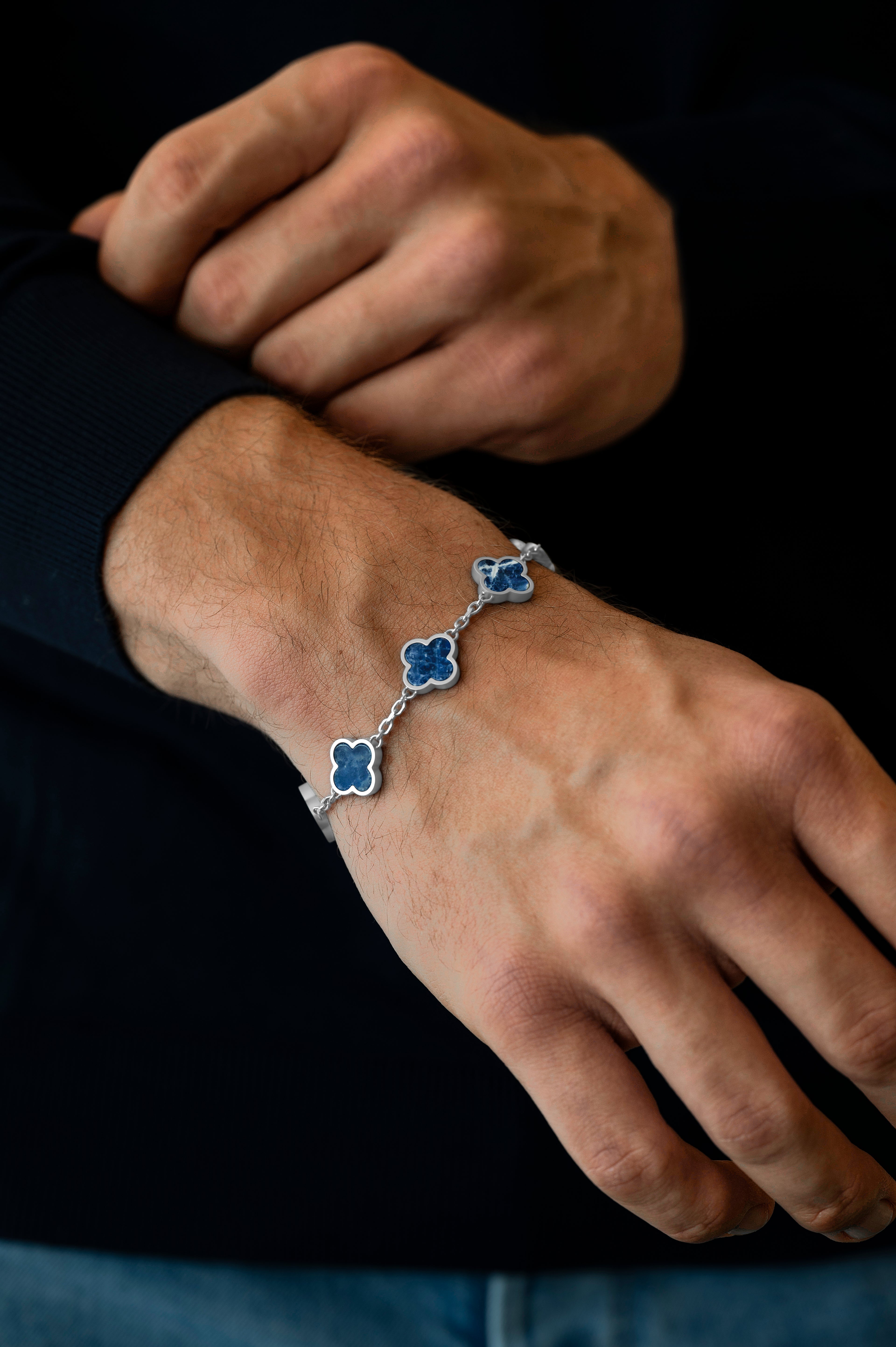 Hand wearing a blue floral bracelet on a dark background