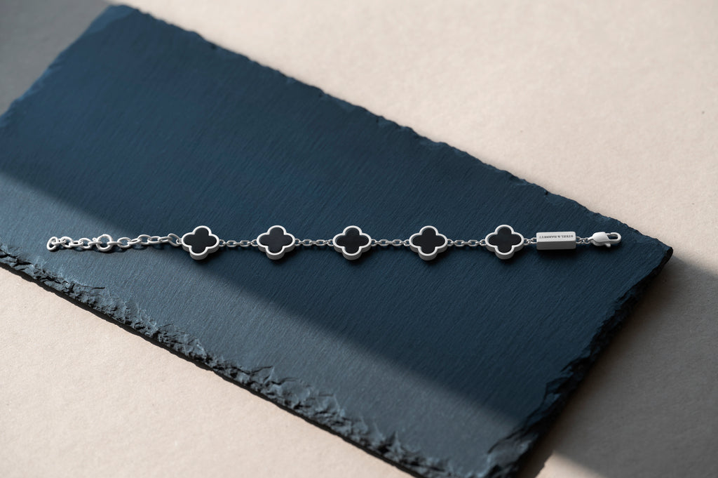 Silver bracelet with clover-shaped links on a dark blue fabric background