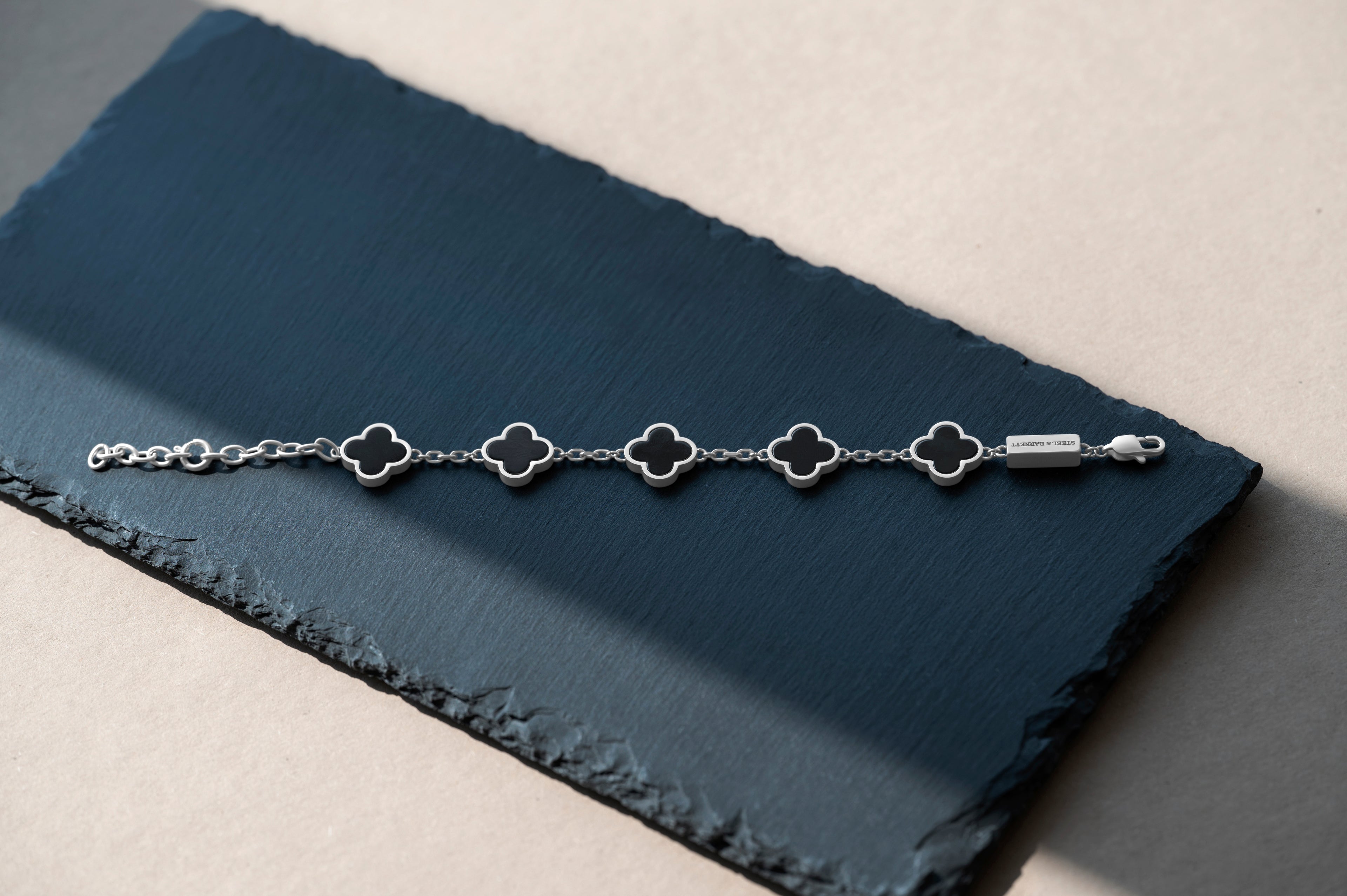 Silver bracelet with clover-shaped links on a dark blue fabric background