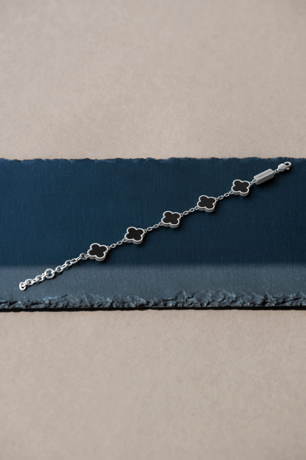 Silver bracelet with clover-shaped charms on a blue and beige fabric background