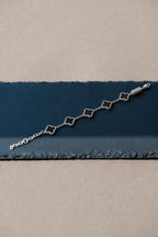 Silver bracelet with clover-shaped charms on a blue and beige fabric background