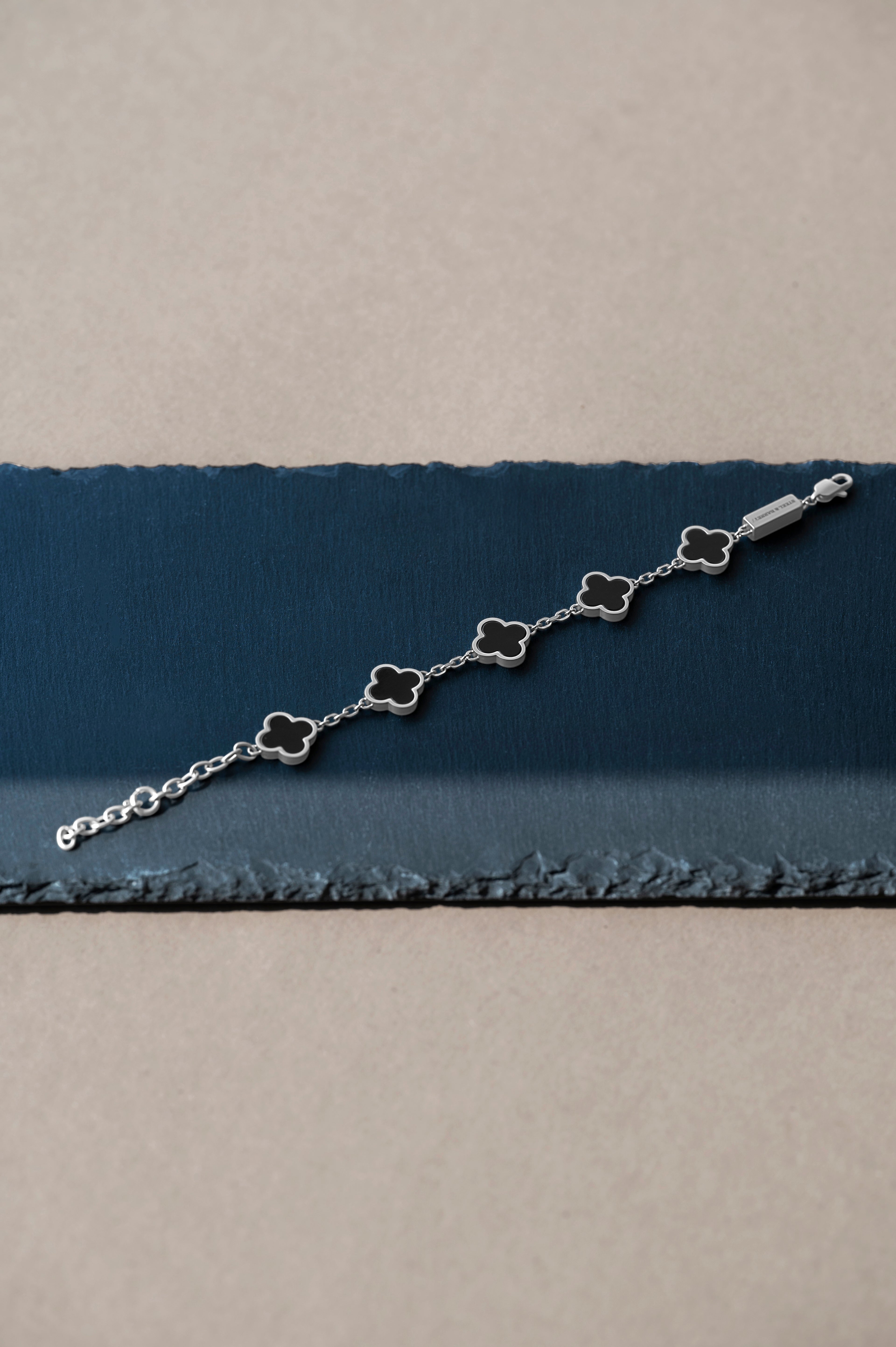 Silver bracelet with clover-shaped charms on a blue and beige fabric background